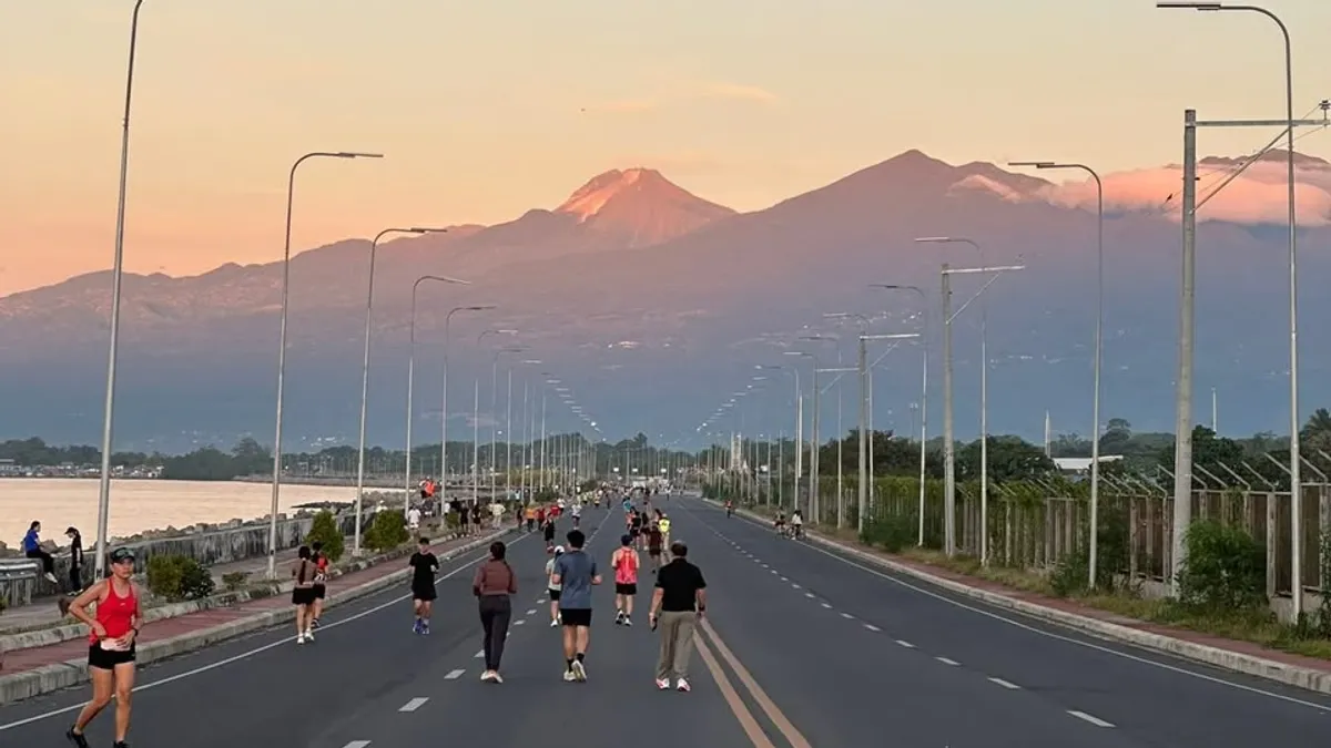 Runners on the coastal road at dusk with a mountain range catching the last light across the gulf