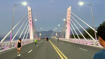 Walkers and runners on a cable-stayed bridge deck at first light, white pylons overhead