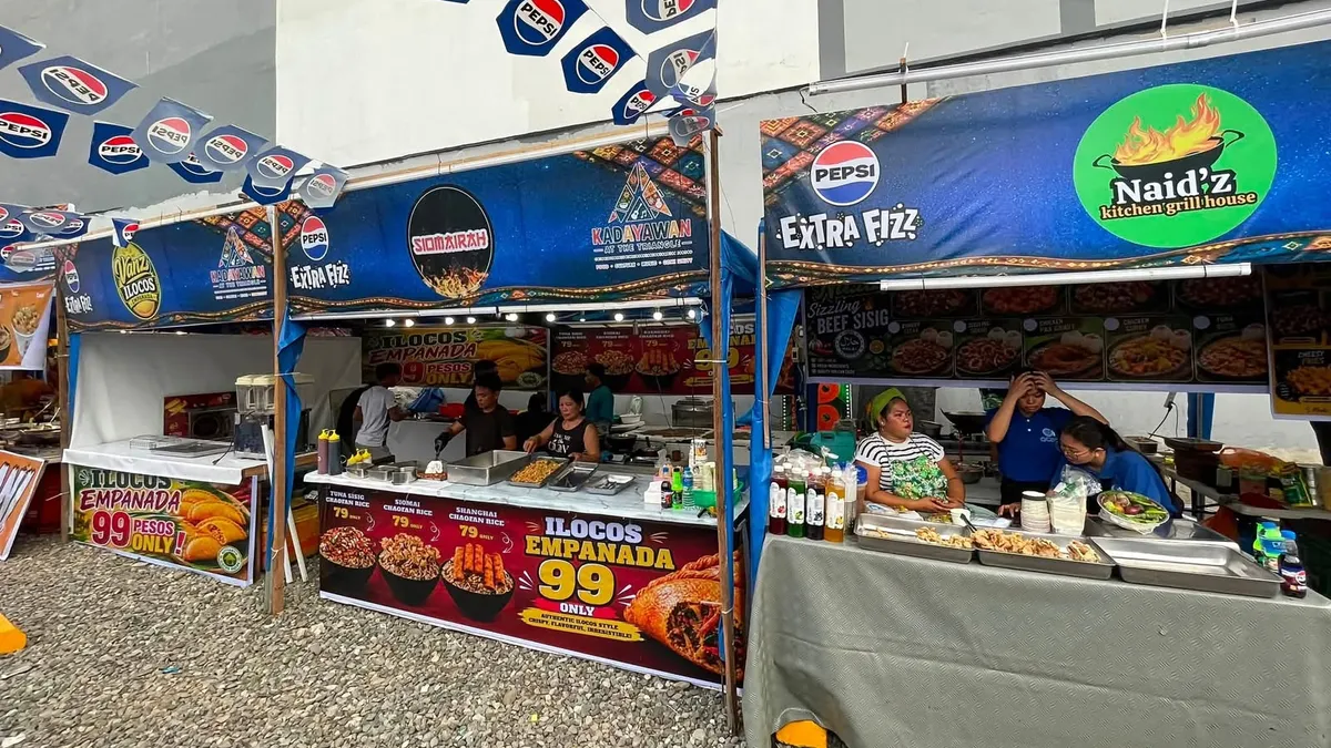 Food festival stalls with a 99-peso empanada price board and vendors serving