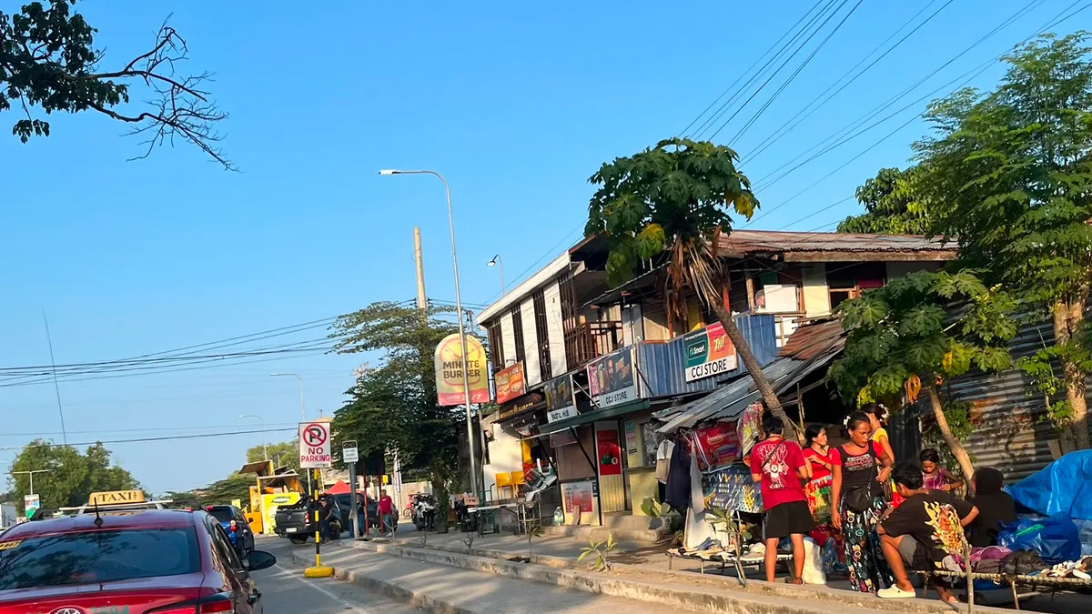 Vendors sitting outside roadside timber shops as a taxi passes