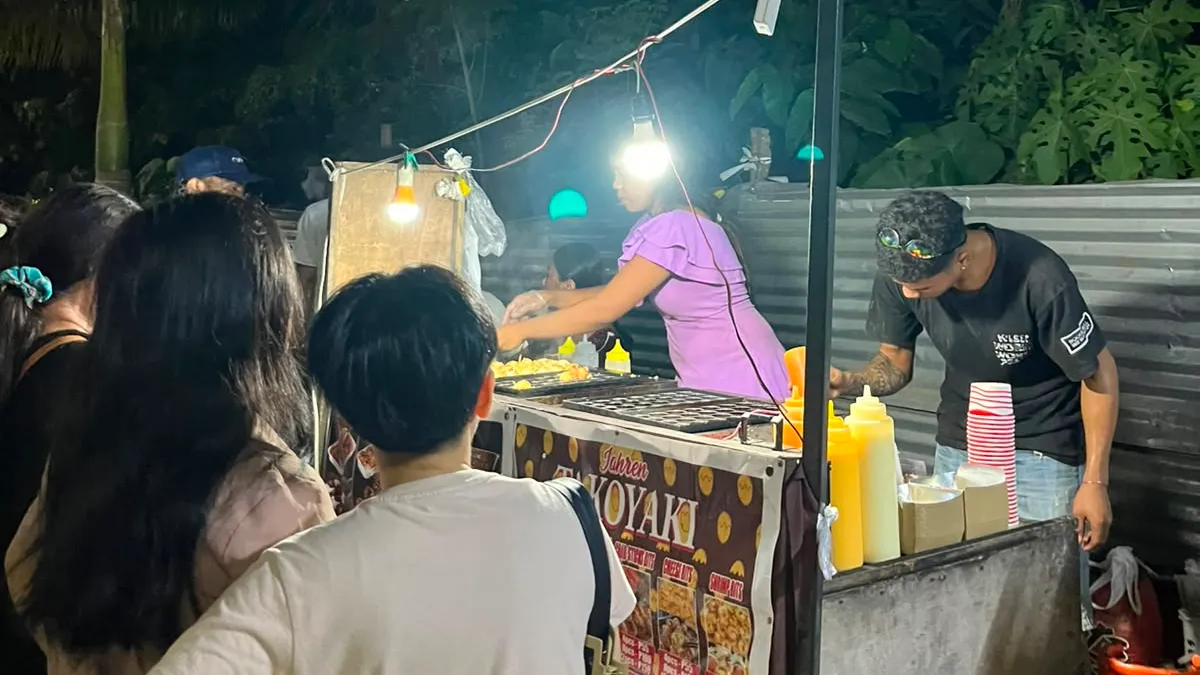 A night street-food cart cooking takoyaki for a small crowd of customers in Davao