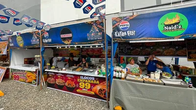 Food festival stalls with a 99-peso empanada price board and vendors serving