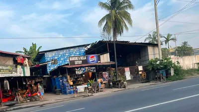 Roadside carinderia under a tall palm with customers at the counter