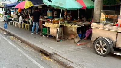Sidewalk fruit and snack stalls under patched umbrellas beside a wooden cart