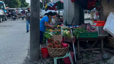Sidewalk vegetable and fruit stall set up against a concrete flyover column