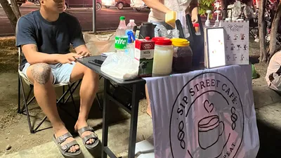 Two vendors running a pop-up street coffee stall on the pavement at night