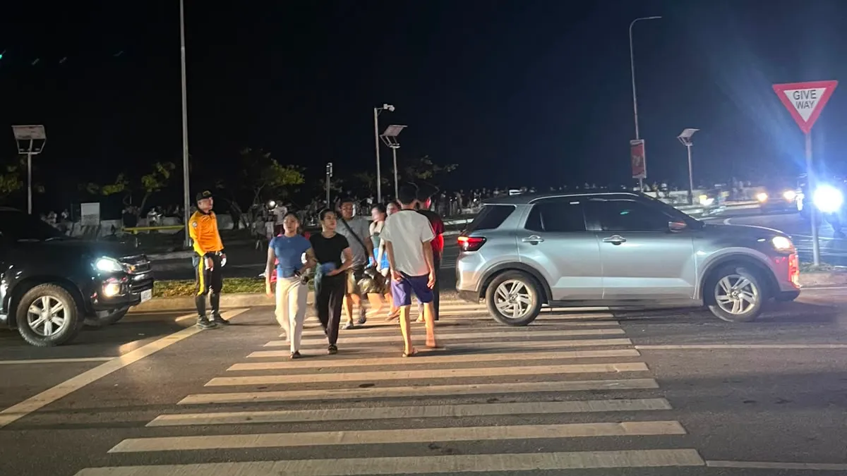 People crossing a lit road at night in front of waiting cars