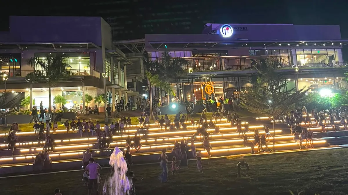 Lit lifestyle mall at night above a lawn and illuminated fountain