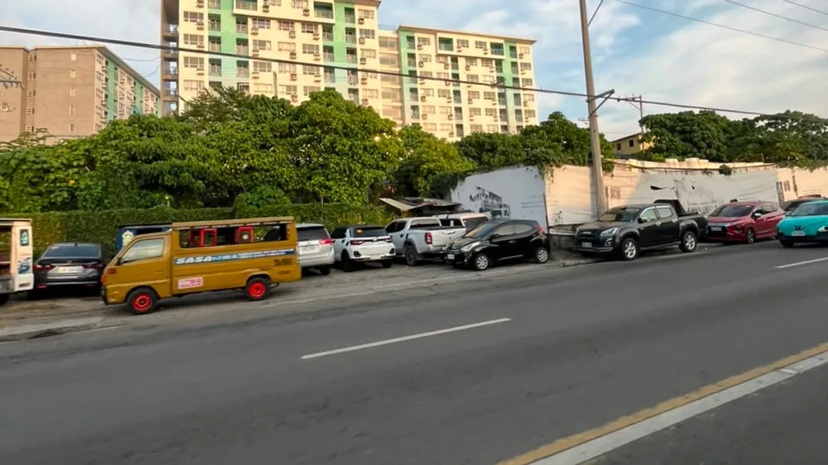 Green and white mid-rise condominium above the treeline with a jeepney parked below