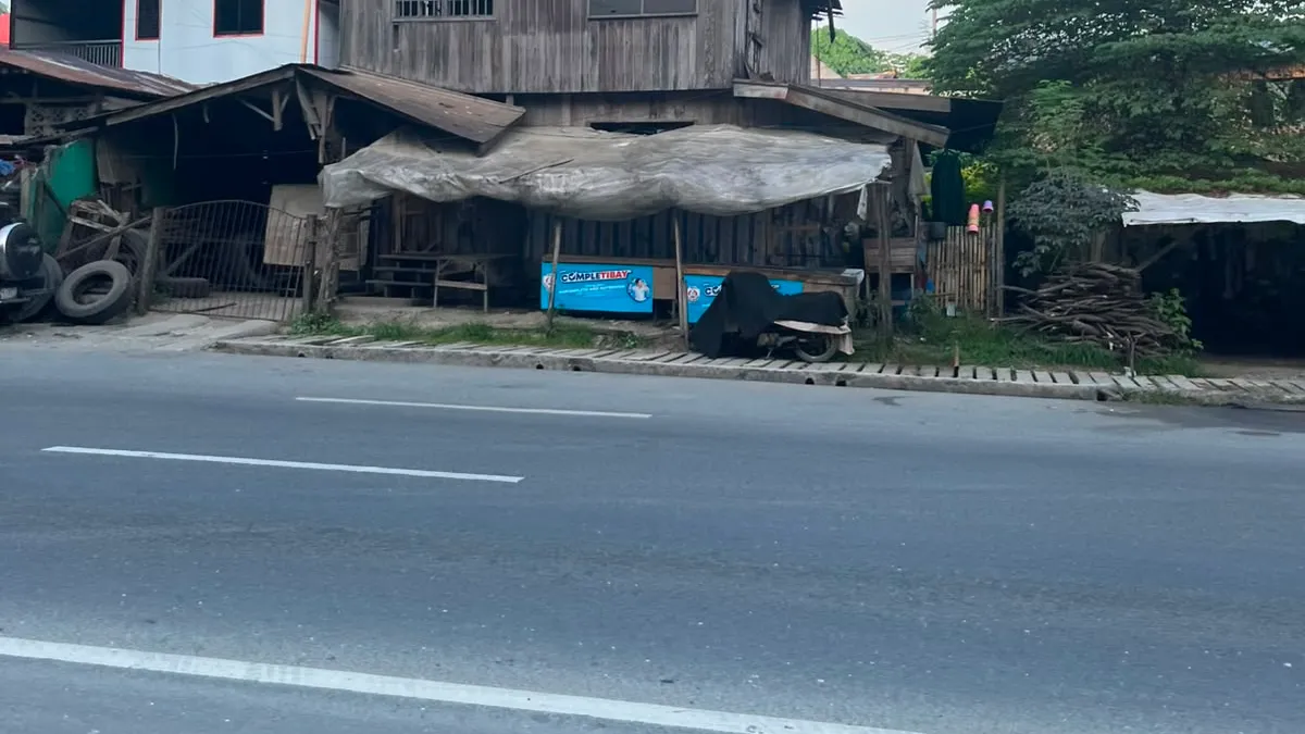 Weathered two-storey timber house with a rusted roof standing beside the road