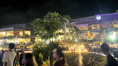 People walking the lawn in front of a lit lifestyle mall at night