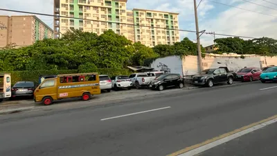 Green and white mid-rise condominium above the treeline with a jeepney parked below