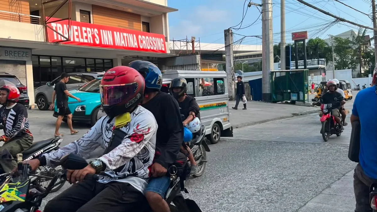 Motorcyclists waiting at Matina Crossing below a traveller's inn sign