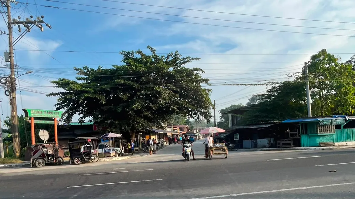 Suburban highway with tricycles waiting outside a row of small shops