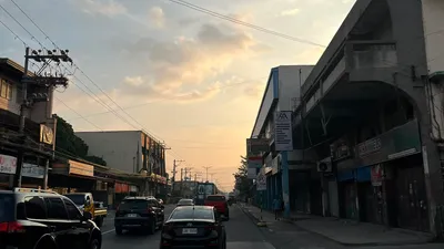 A Davao city street at dawn lined with low buildings and passing cars