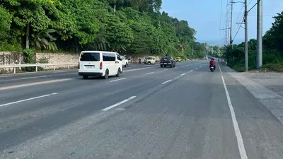 Van on a highway running below a steep forested hillside