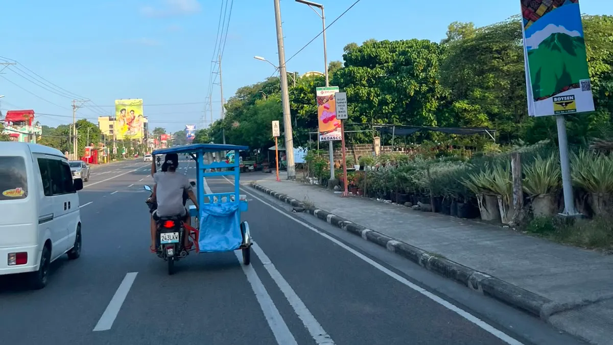 A solar-powered street light over a Davao highway with a pedicab passing below