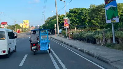 A solar-powered street light over a Davao highway with a pedicab passing below