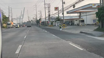 Highway running toward port gantry cranes with a fuel station on the right