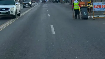 Road works in progress with a hi-vis worker and a slow-down sign on a city road